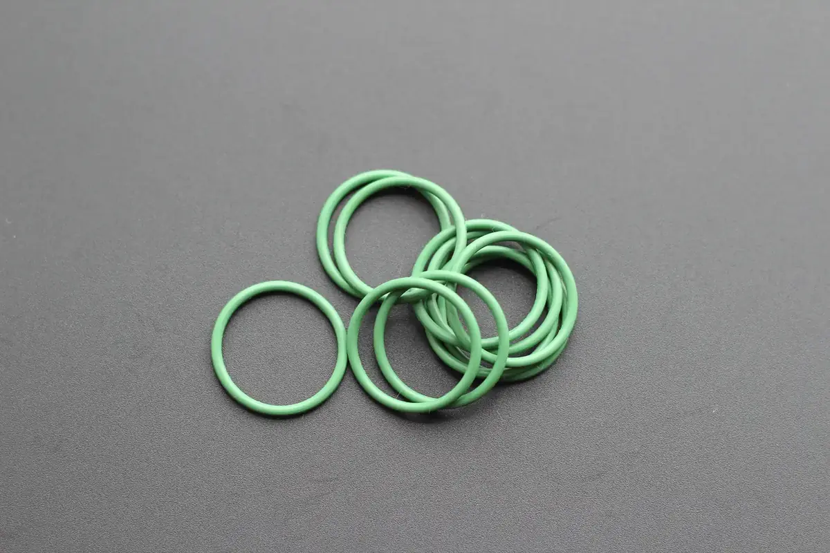 Green perfluoroelastomer O-rings arranged on a grey studio background