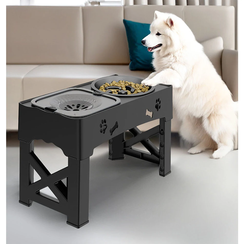 Black elevated dog bowl stand with paw and bone cutouts and two stainless steel bowls, one containing kibble, with a white dog