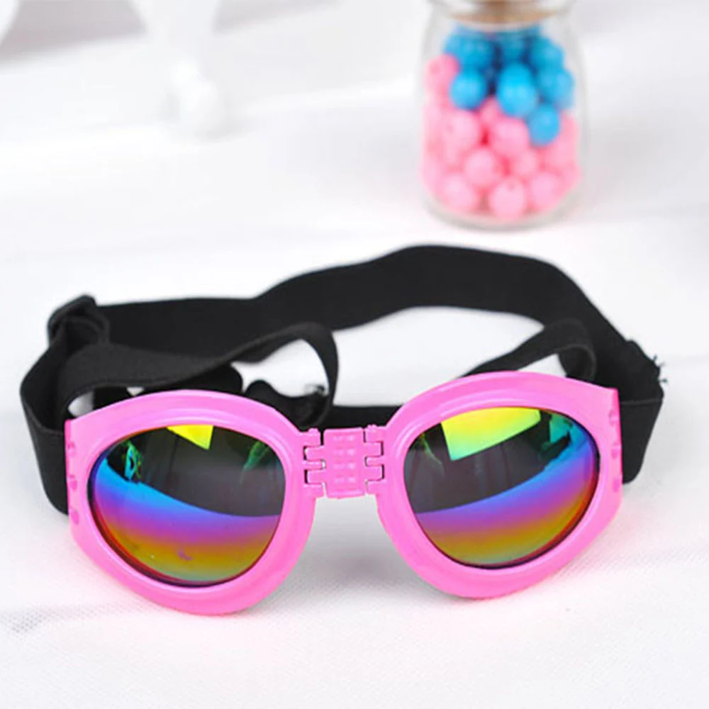 Pink goggles with rainbow reflective lenses and a black strap resting on a white surface