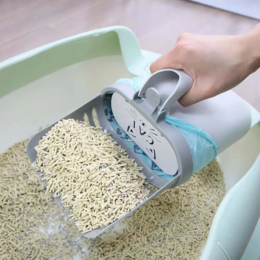 A hand holding a gray cat litter scoop filled with pellets over a mint green litter box.