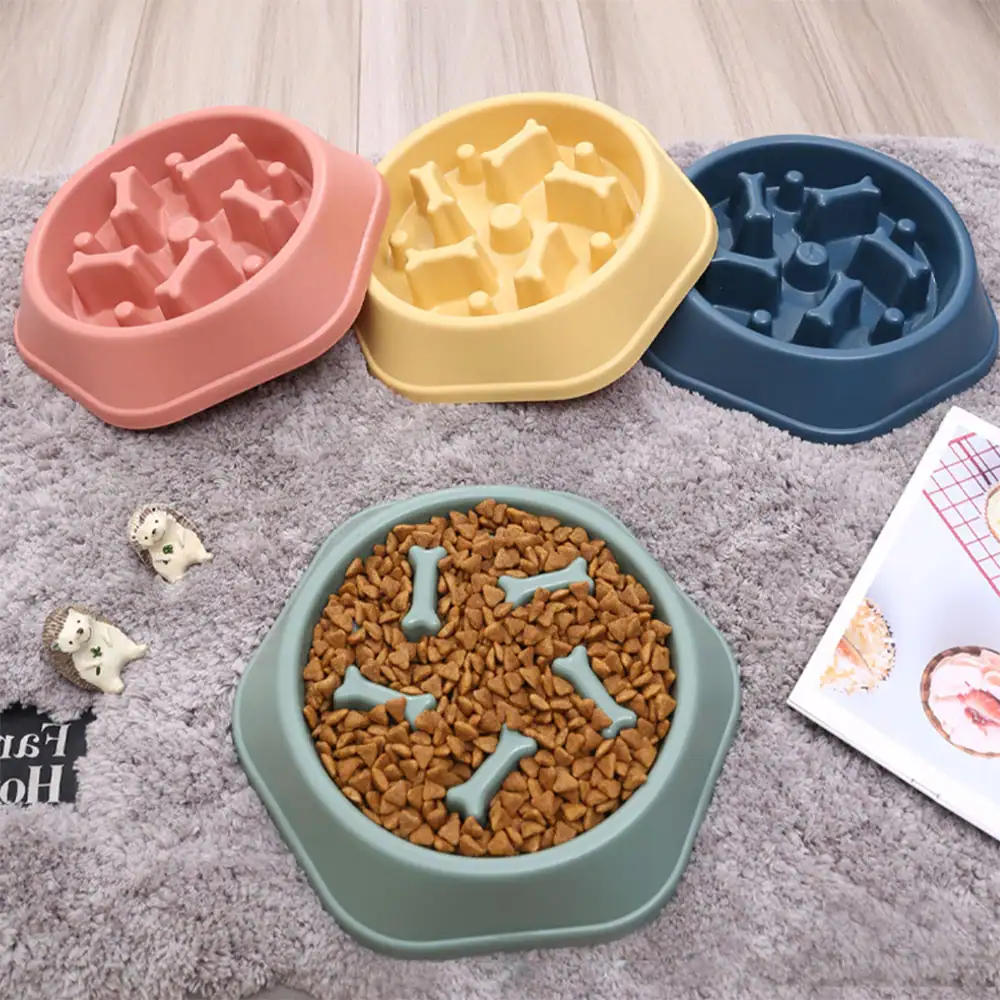 Four colorful slow feeder bowls arranged on a gray rug, one filled with kibble.