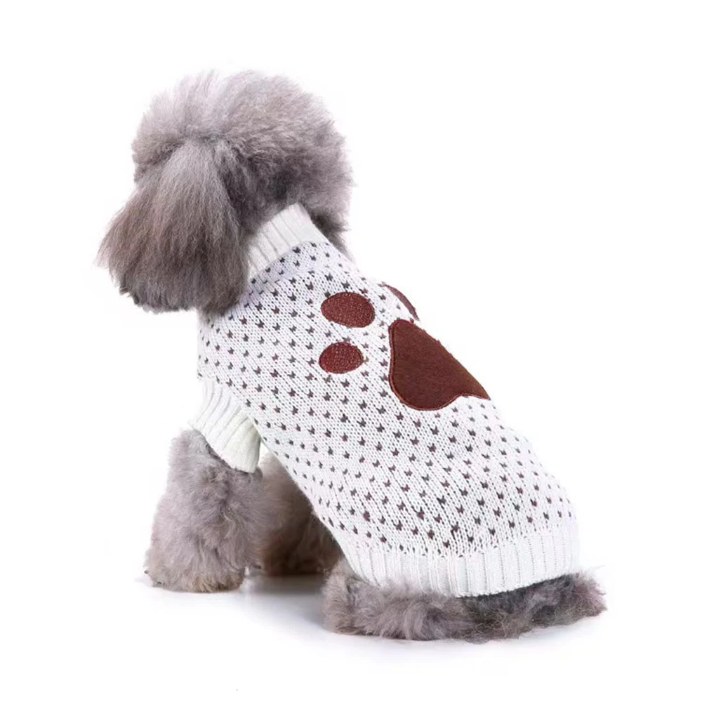 A grey poodle wearing a white knitted sweater with a brown paw print design on the side.