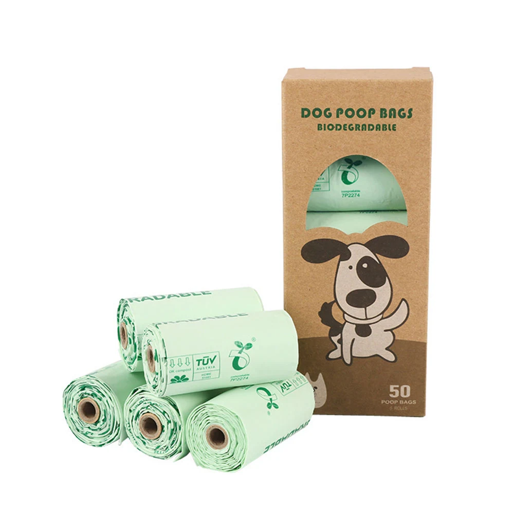 Stack of green biodegradable dog poop bag rolls next to a brown cardboard box with a cartoon dog illustration.