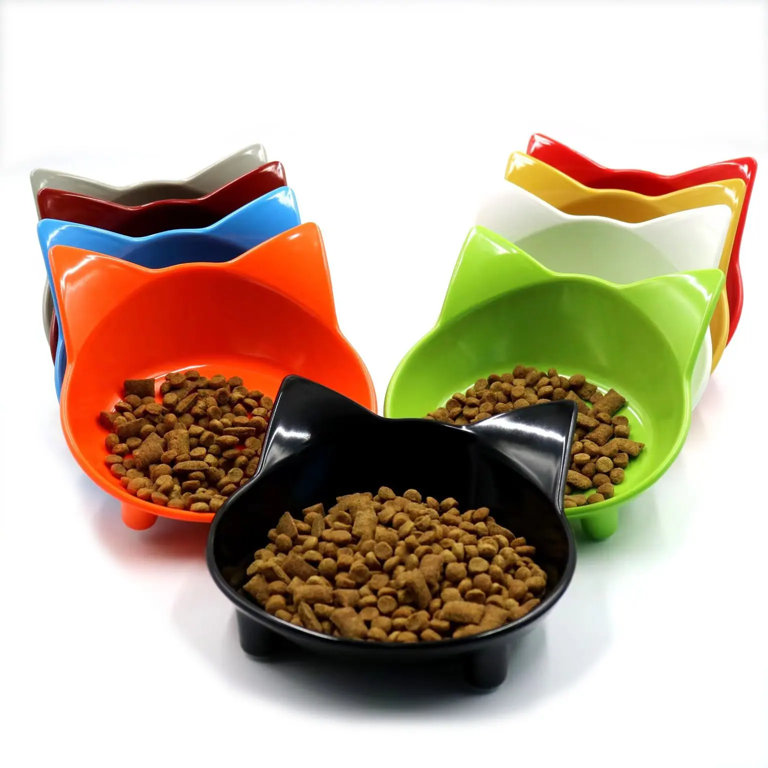 Multiple colorful cat-shaped ceramic bowls filled with dry pet food arranged on a white background