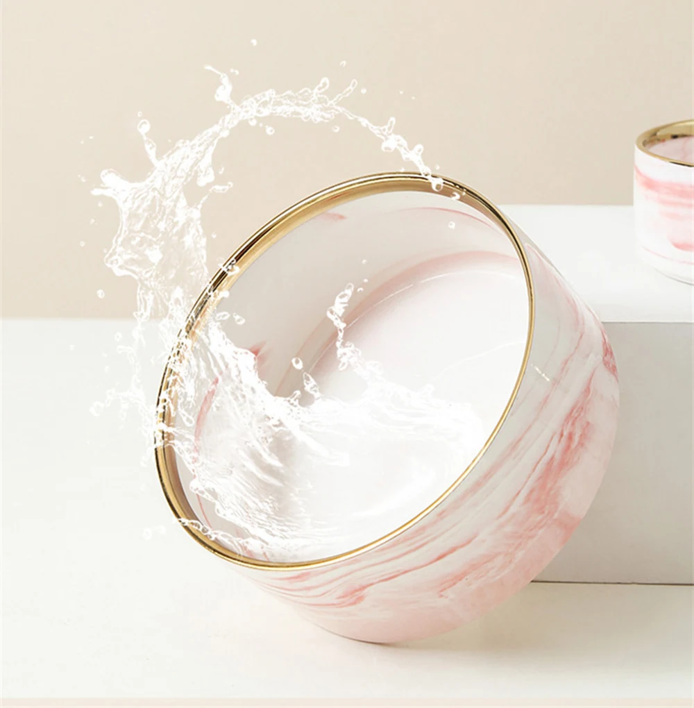 A pink and white marble patterned bowl with a gold rim and a splash of water inside.