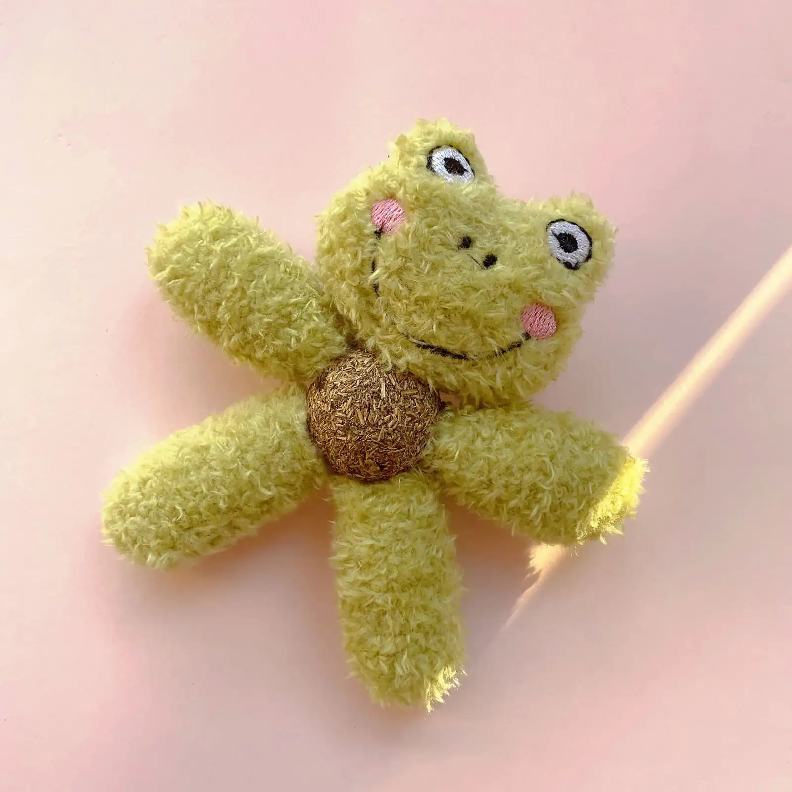 A yellow plush frog toy with a brown center on a pink background