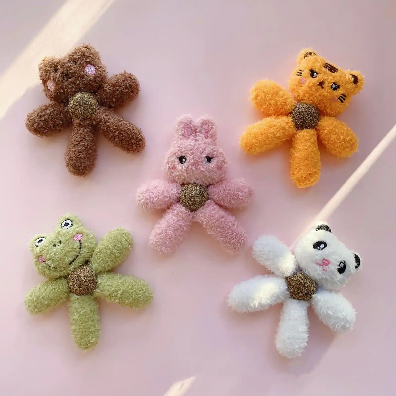 Five plush animal hair clips shaped like a bear, tiger, rabbit, frog, and panda on a pink background