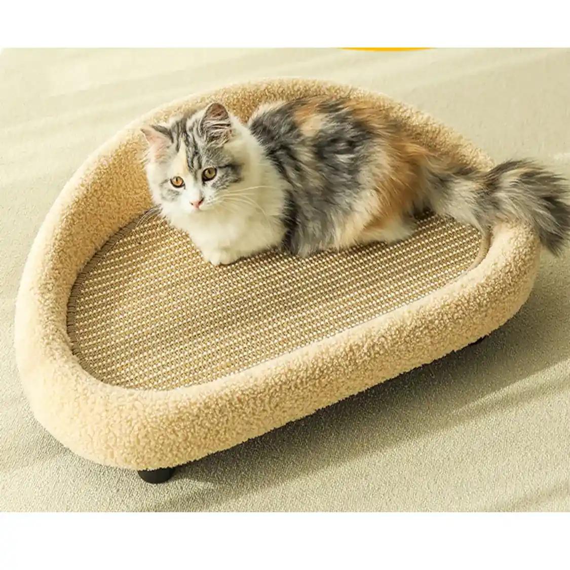 A fluffy calico cat lying on a beige, oval-shaped pet bed with a textured scratching surface.