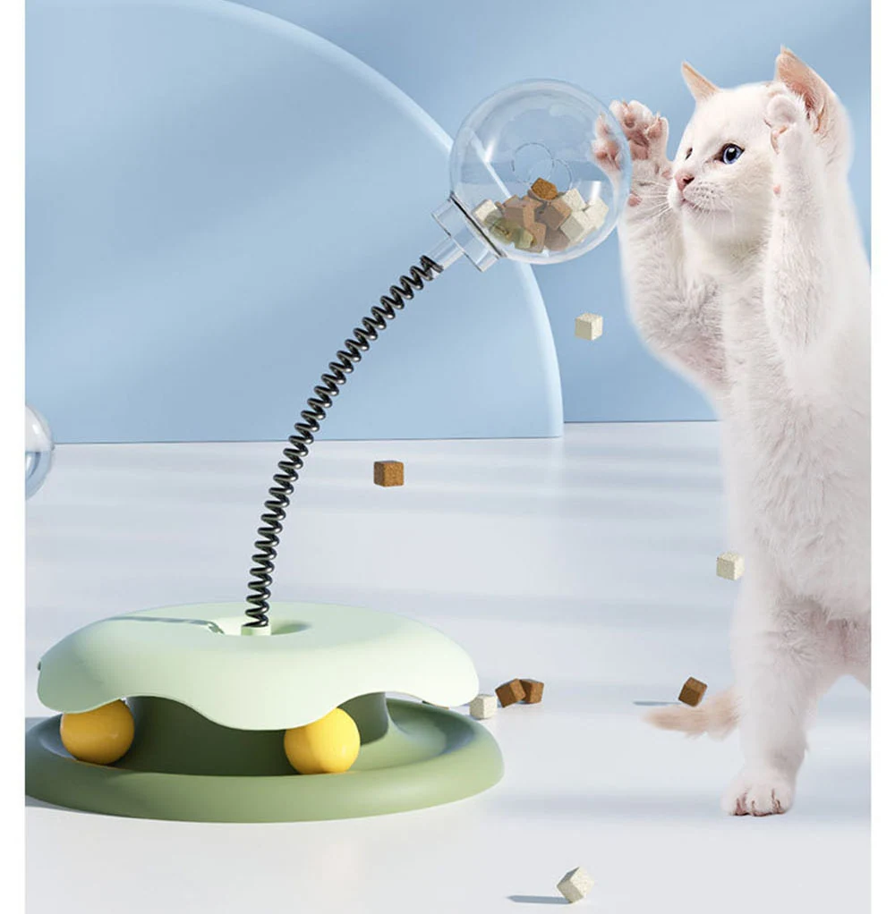 A white cat stands on hind legs to bat at a spring-loaded treat dispenser toy.