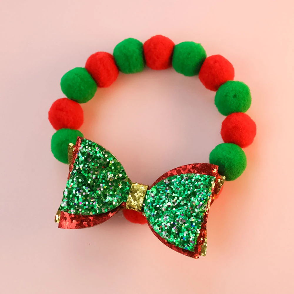 Christmas headband featuring red and green pom-poms and a glittery sequin bow on a pink background.