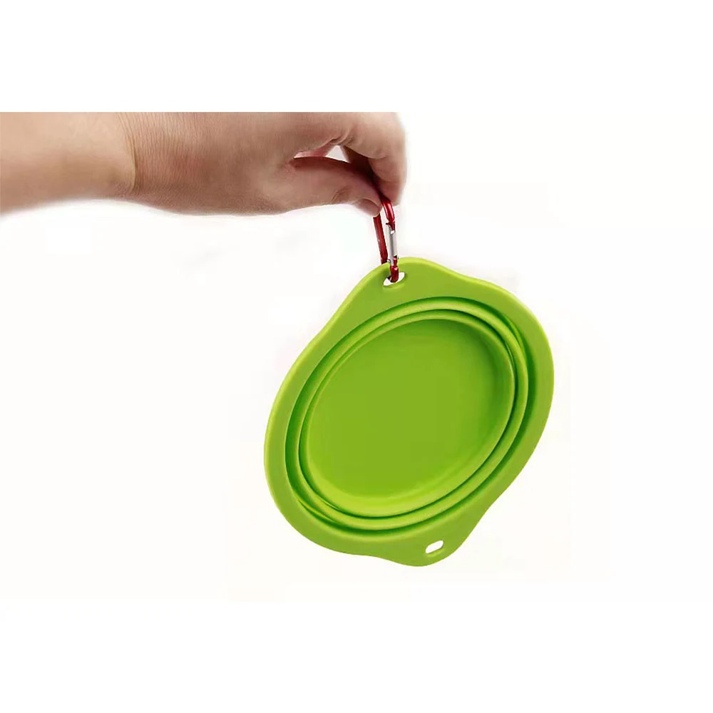 A hand holding a collapsed green silicone bowl with a red carabiner attached.
