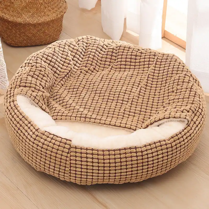 Round beige textured pet bed with white sherpa lining sitting on a light wooden floor