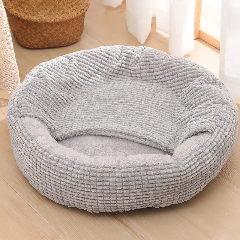 A gray, textured, circular pet bed sitting on a light wooden floor.