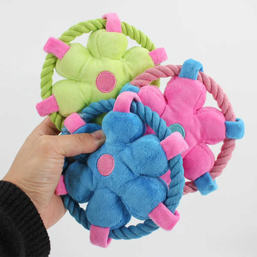 A hand holding three plush flower-shaped dog toys with attached rope rings in green, pink, and blue.
