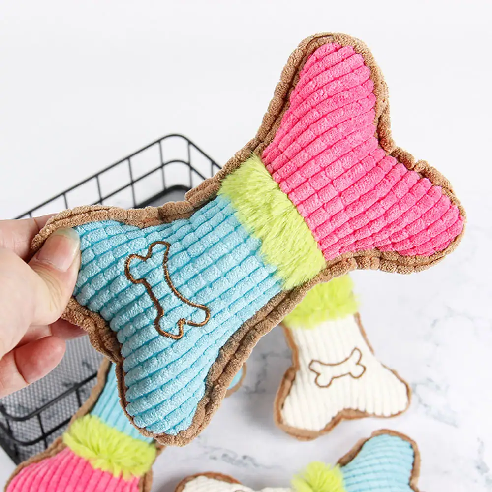 Hand holding a blue, lime, and pink corduroy dog toy shaped like a bone with a stitched bone icon.