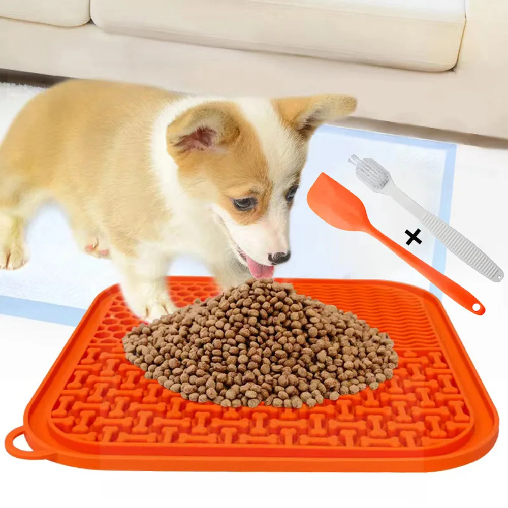 Orange silicone slow feeder mat with dry food and a corgi, accompanied by a spoon and cleaning brush.