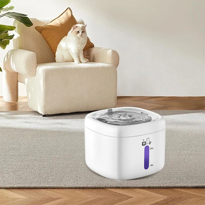 A white pet water fountain sits on a rug in the foreground with a cat on an armchair in the background.