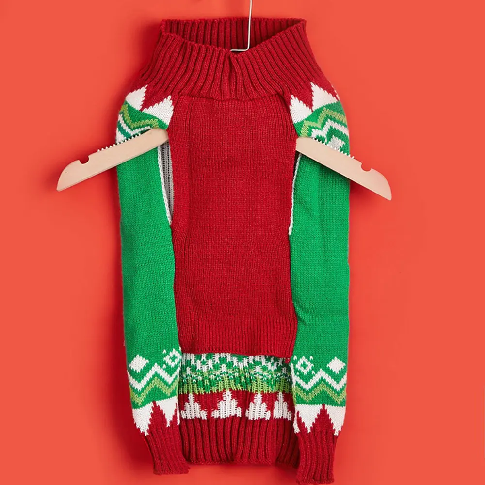 Red and green knitted sweater with festive patterns hanging on a wooden hanger against a red background