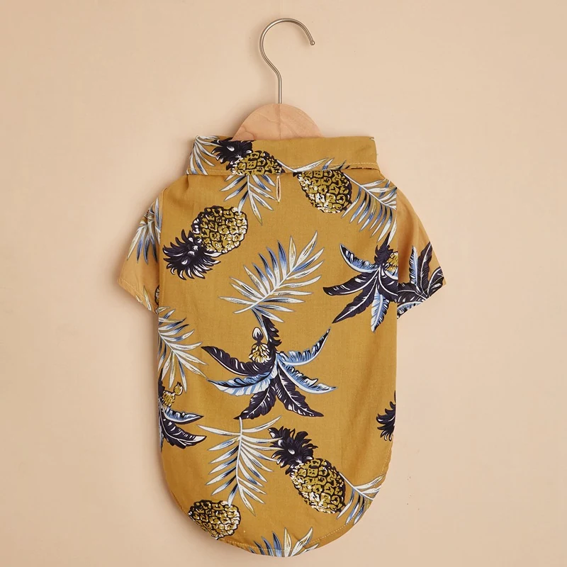 Yellow short-sleeved pet shirt with a pineapple and palm leaf print hanging on a wooden hanger