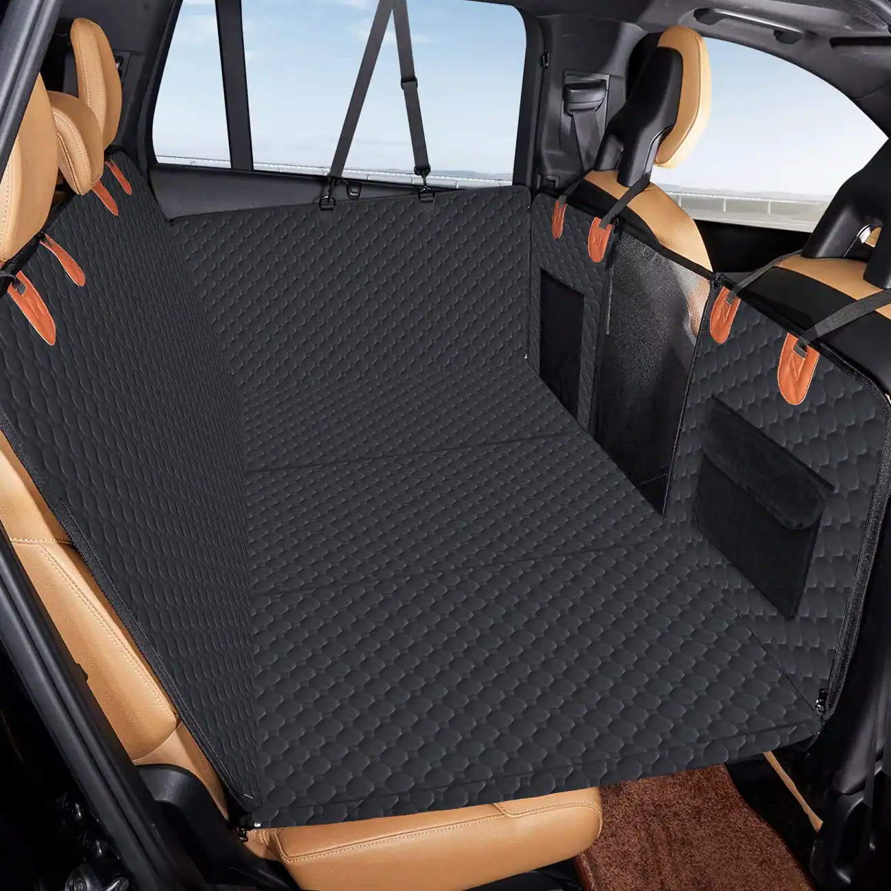A black quilted car seat extender installed in the back of a vehicle with tan leather seats.