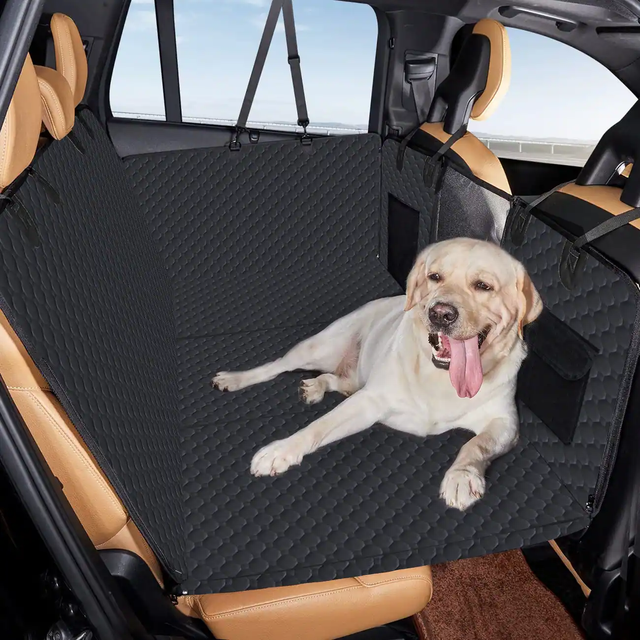 A light-colored dog lying on a black quilted car seat cover installed in the back of a vehicle.
