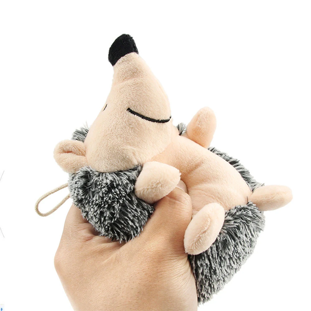 A hand holding a beige and grey plush hedgehog toy with a cord loop.