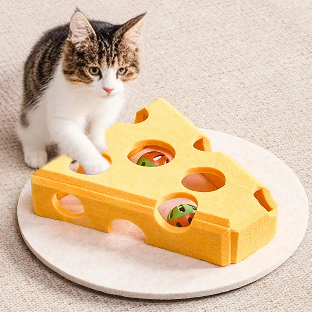 A cat plays with a yellow, cheese-shaped puzzle toy containing balls.
