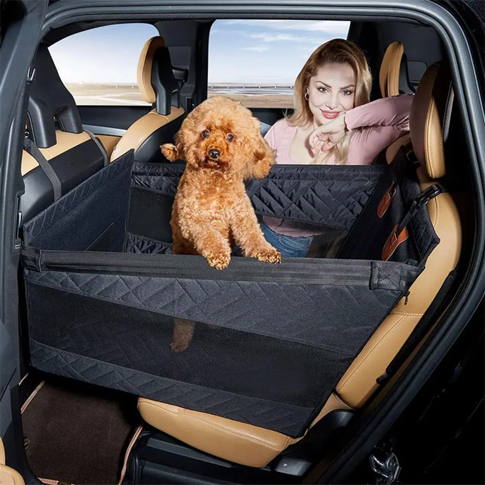 A brown poodle sitting in a black quilted dog car seat booster installed in a vehicle.