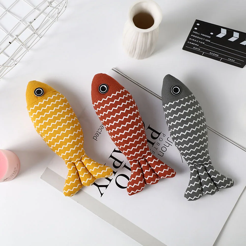 Three plush fish toys with zigzag patterns in yellow, red, and grey arranged on a white surface.