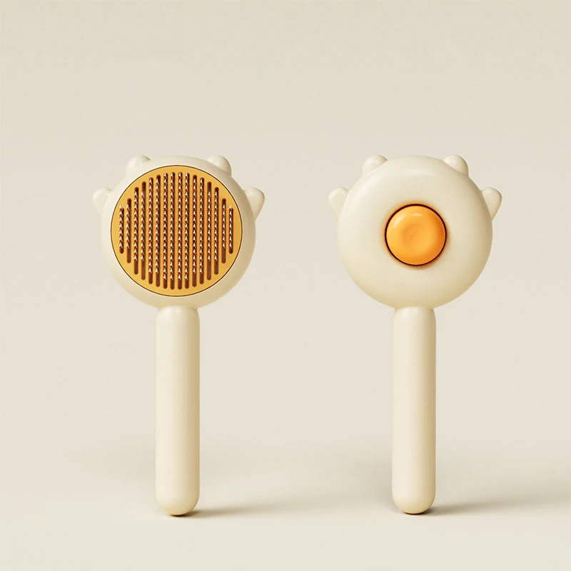 Front and back view of a cream-colored cat-shaped pet grooming brush with orange bristles on a beige background