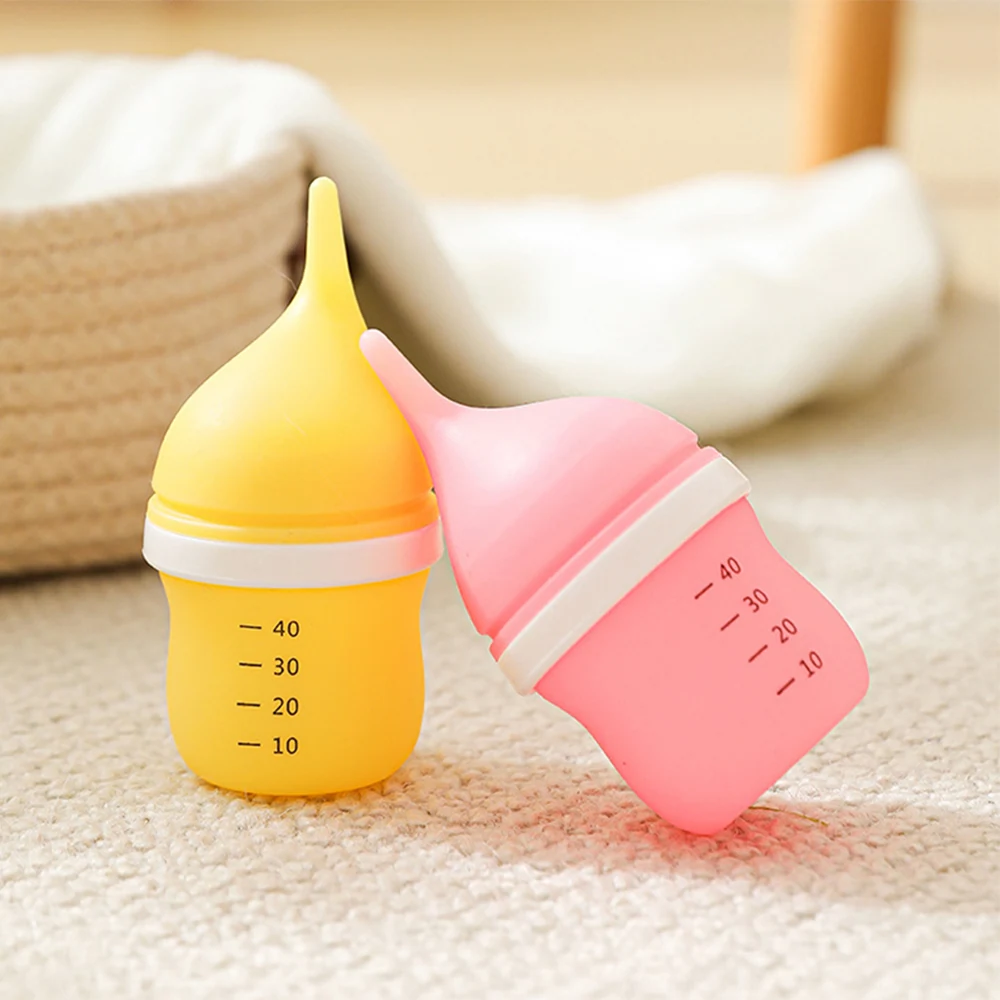 Yellow and pink silicone baby feeding bottles with measurement markings resting on a soft, neutral surface