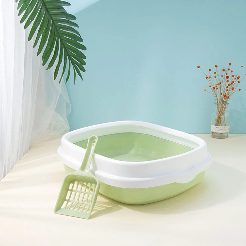 A light green and white plastic litter box with a matching scoop sitting on a table.