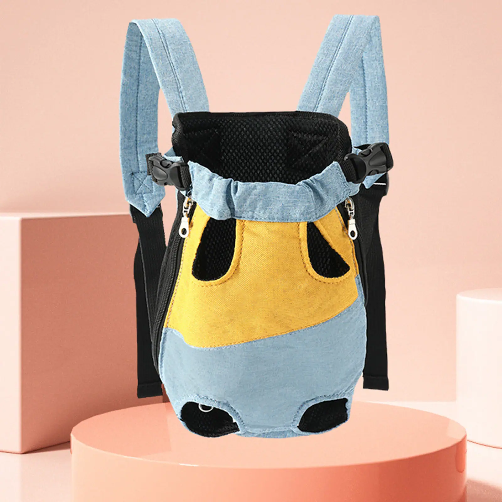 Blue and yellow denim baby carrier with black mesh straps and buckles displayed on a pink pedestal
