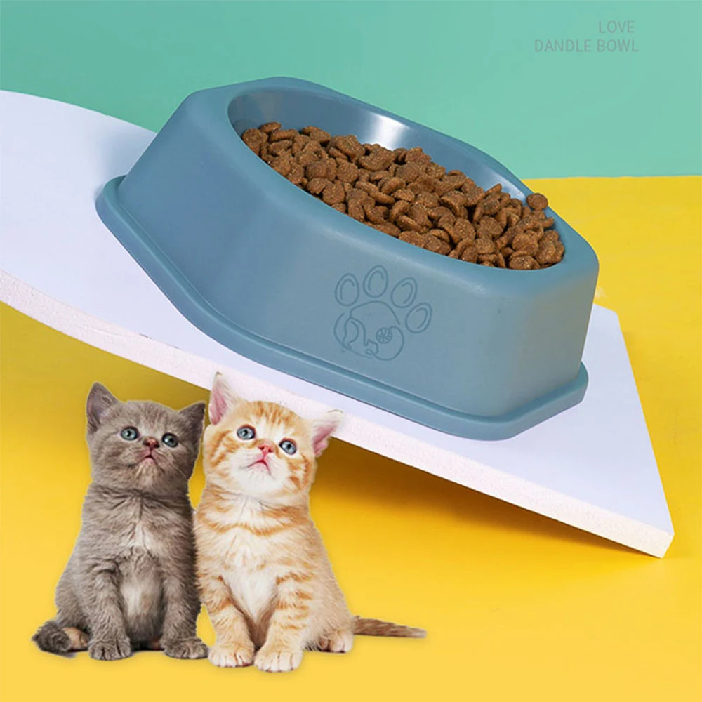 Blue tilted pet food bowl filled with kibble, positioned above two kittens looking up.