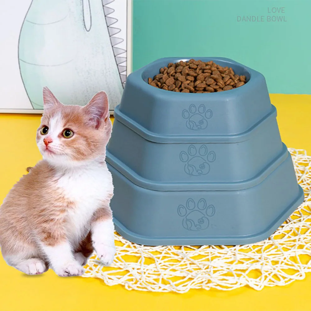 A blue tiered cat bowl filled with food sits next to a kitten on a yellow background.