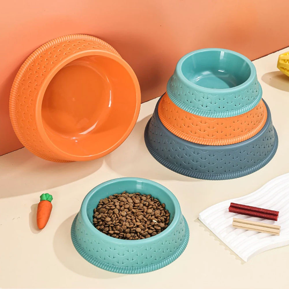 A stack of orange, blue, and teal pet bowls next to a filled teal bowl and a carrot toy.