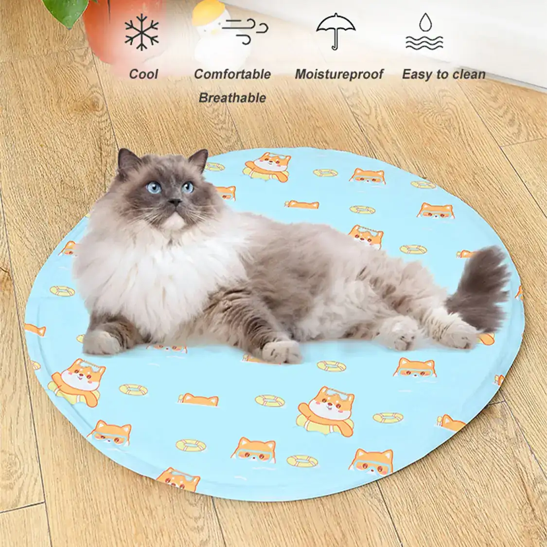 A fluffy cat lying on a round blue cooling mat with orange cat patterns on a wooden floor