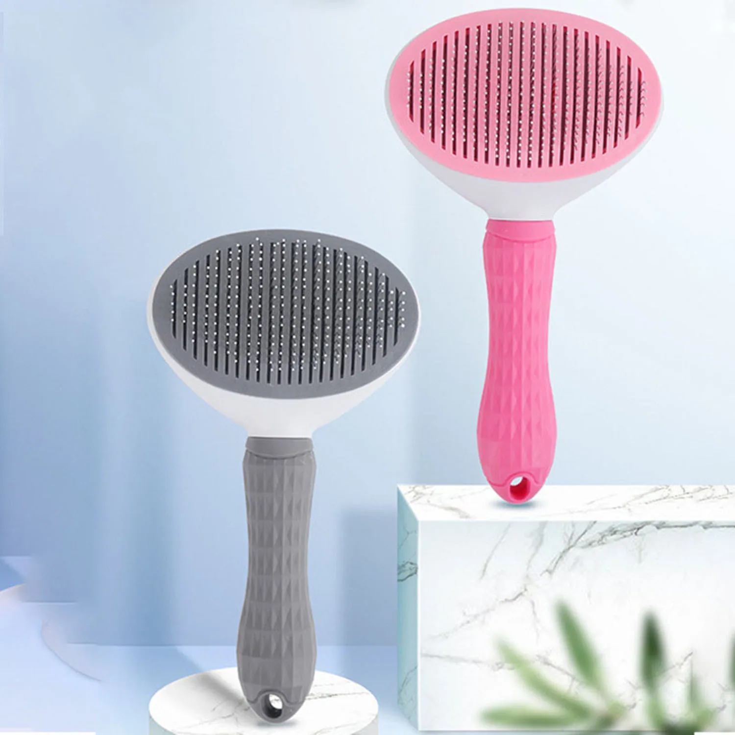 Two oval grooming brushes, one pink and one gray, displayed on white marble pedestals.