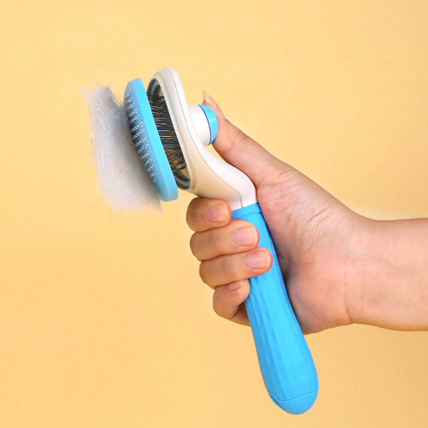 Hand holding a blue and white pet grooming brush with collected fur against a yellow background
