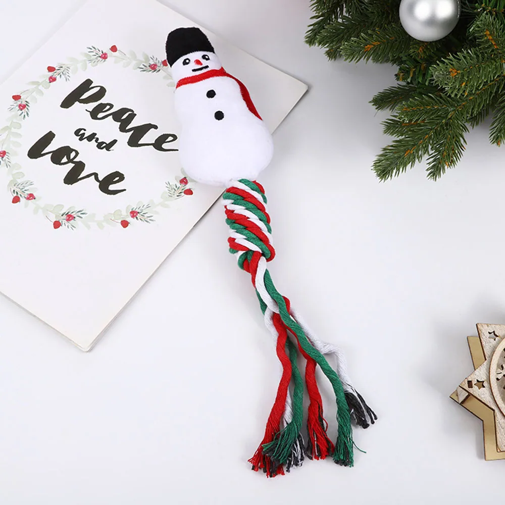 A plush snowman cat toy with red, green, and white rope tail next to a Christmas card and pine branches.
