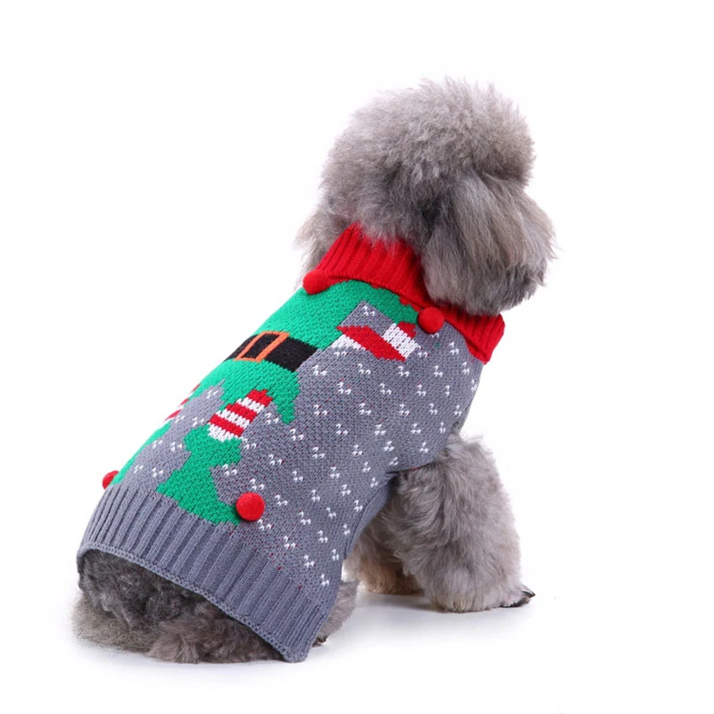 A gray poodle wearing a knitted Christmas sweater with a tree design and red pom-poms.