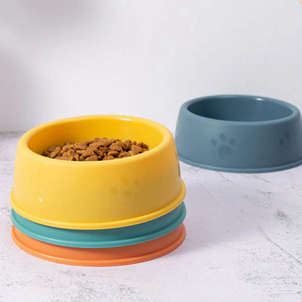 Stacked yellow, teal, and orange pet bowls with kibble, and a separate blue bowl on a light surface.