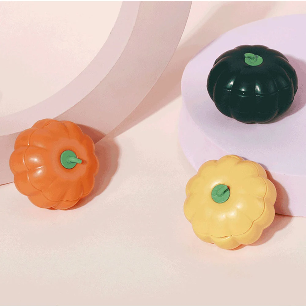 Three small pumpkin-shaped toys in orange, yellow, and dark green arranged on pastel geometric blocks.