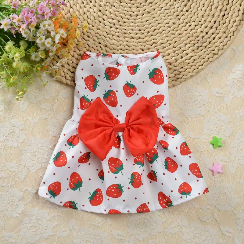 White sleeveless dress with strawberry print and red bow, laid flat on a lace background.