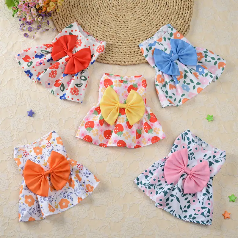 Five floral fabric bibs with large satin bows in red, blue, yellow, orange, and pink arranged on a beige surface.