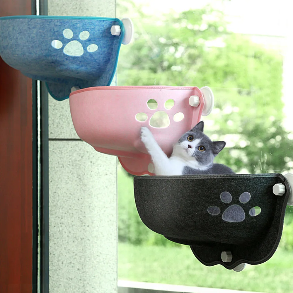 Three felt cat window perches in blue, pink, and black attached to a glass pane, with a kitten in the lower bowl.
