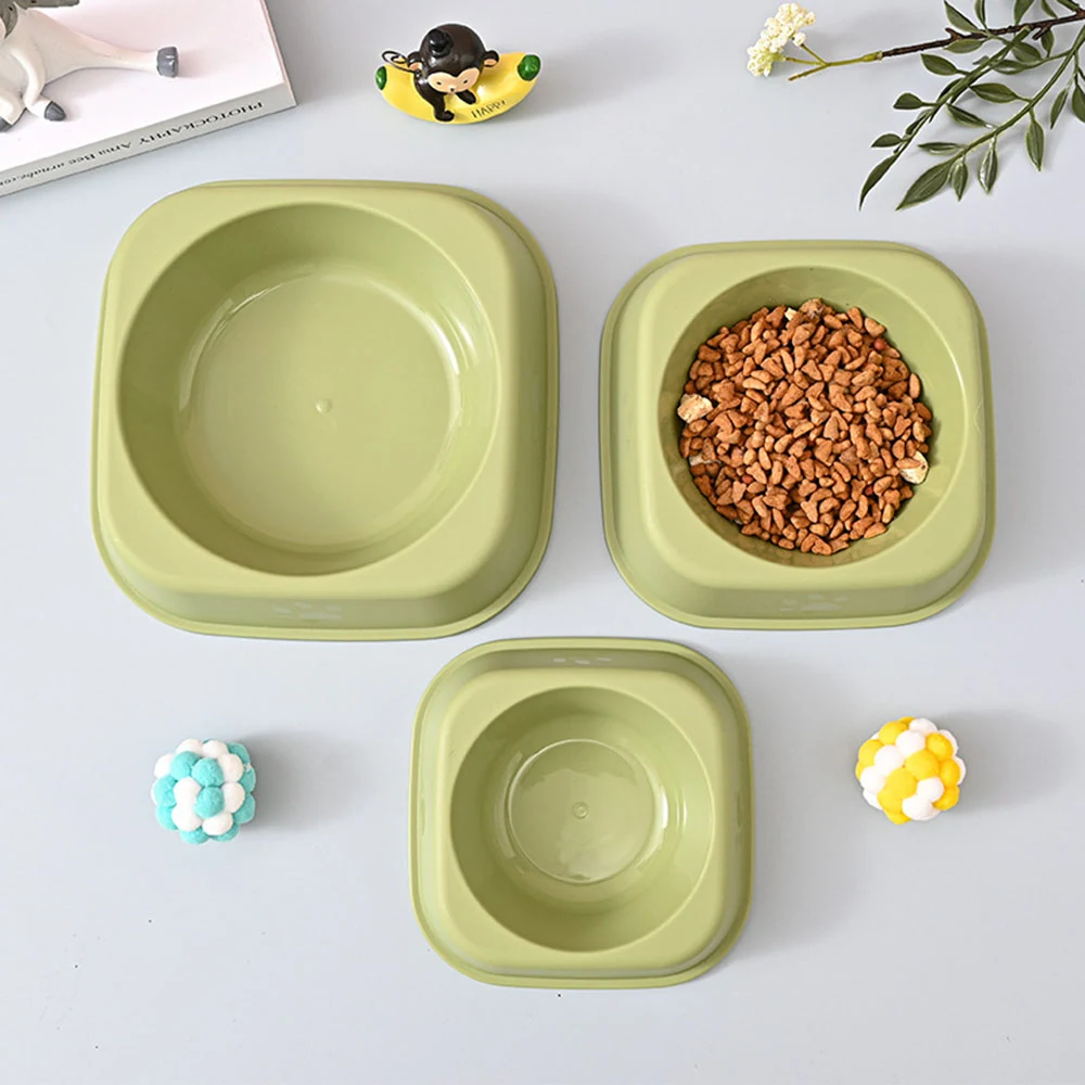 Three sage green ceramic pet bowls arranged on a white surface, one filled with dry kibble.