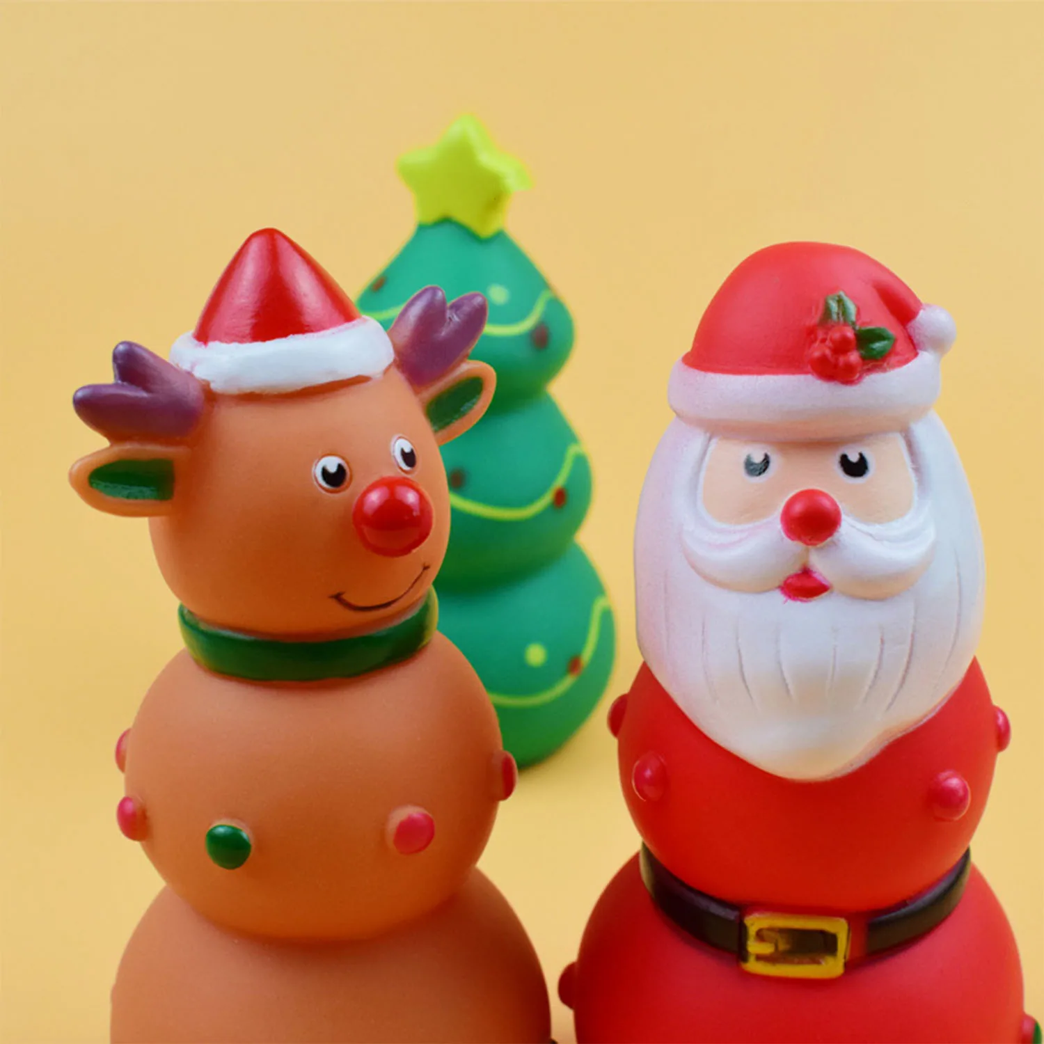 Three plastic Christmas toys: a reindeer, a green tree, and Santa Claus on a yellow background.