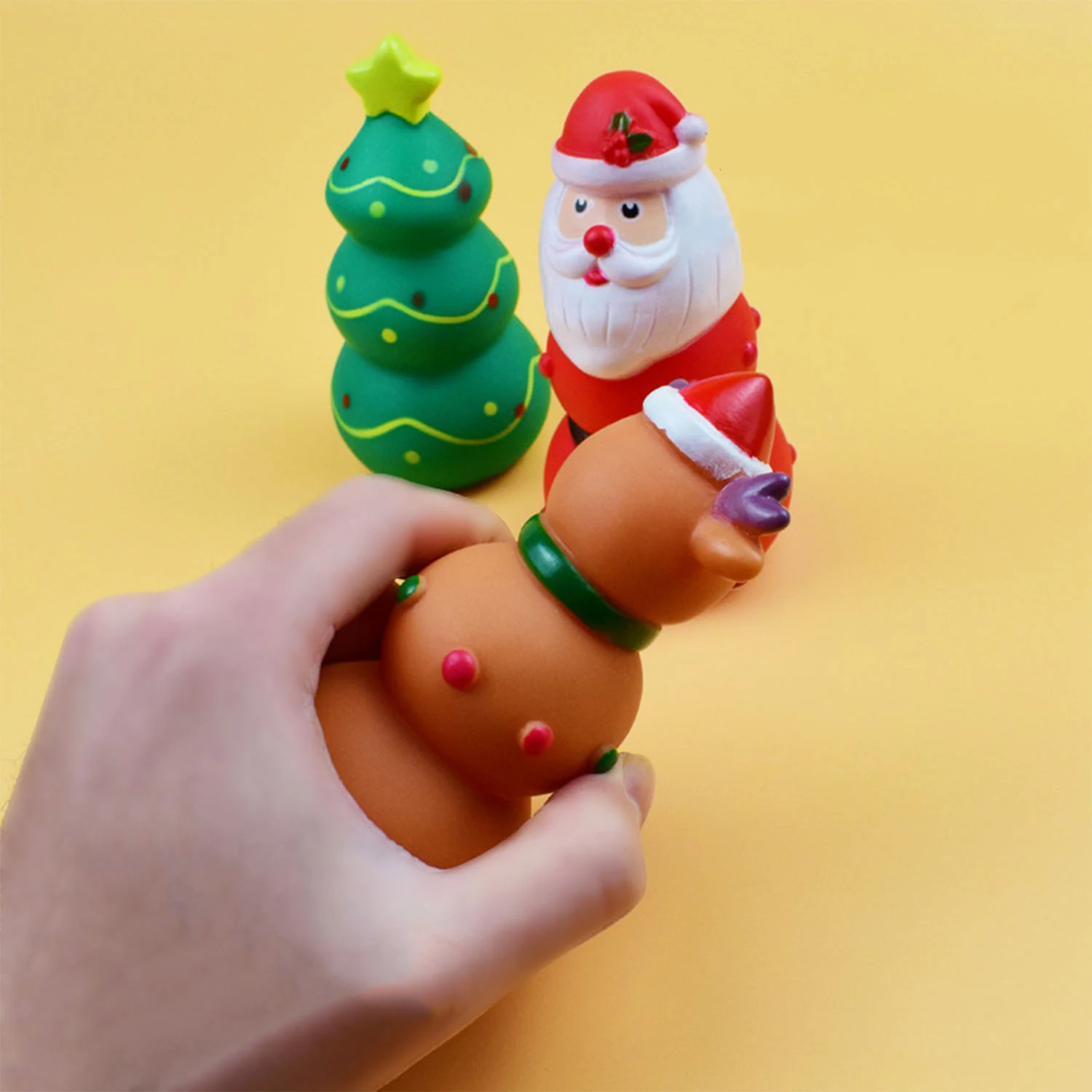 Hand squeezing a brown squishy dog toy with a Santa hat, with a Christmas tree and Santa toy in the background.