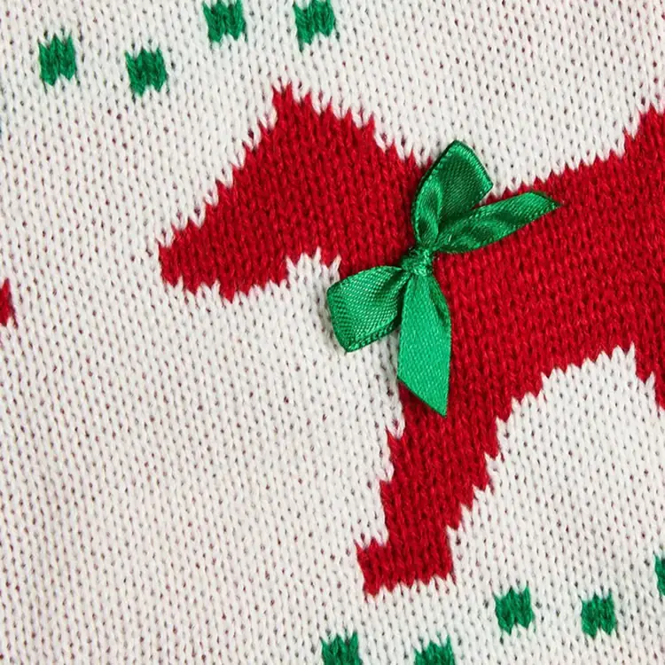 Close-up of white knitted fabric featuring a red dog pattern and a small green satin bow.